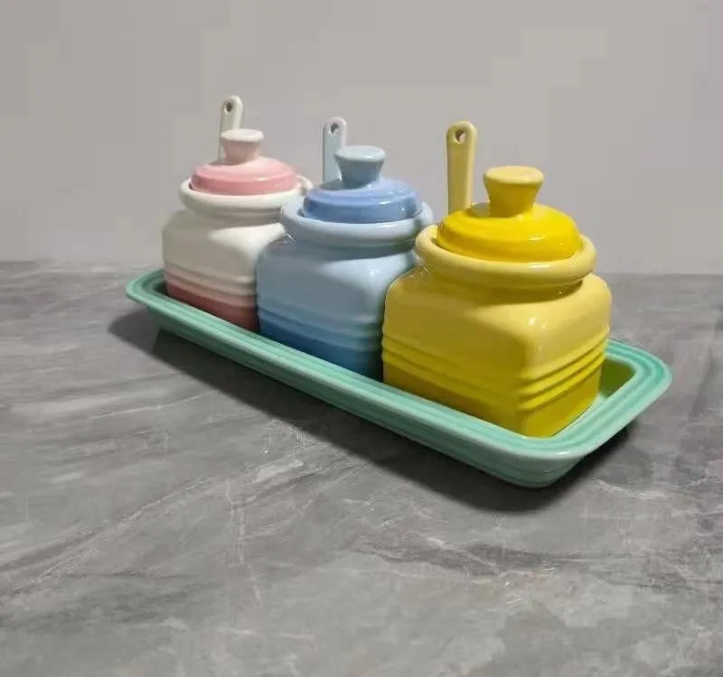 Three cool-coloured ceramic seasoning pots with a matching spoon on a kitchen counter