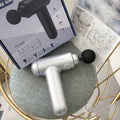 Black handheld fascia gun with massage head on a grey background.