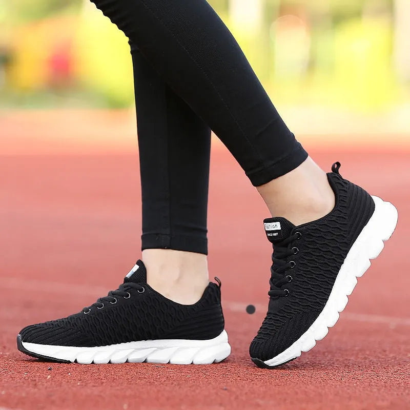Women's black and pink running shoes showing fly weave upper texture and rubber outsole.