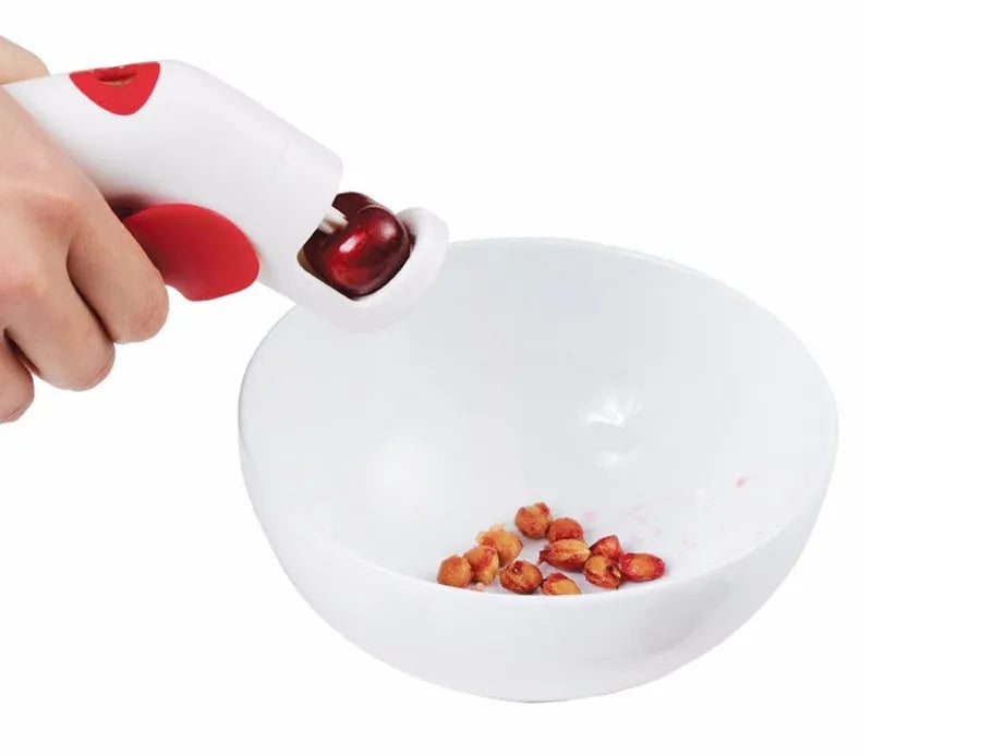 Cherry pitter kitchen tool with soft-grip handle and stainless steel plunger on a plastic base.