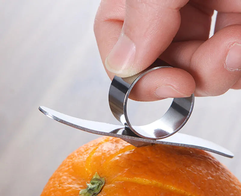 Silver stainless steel finger ring fruit peeler for oranges and pomelos on a kitchen surface.