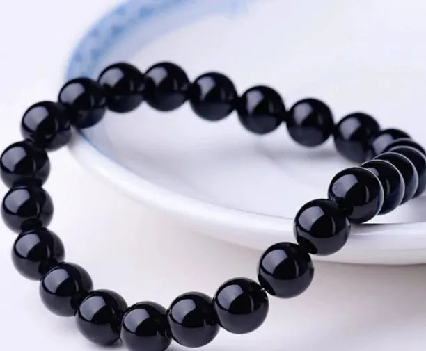 Close-up of a black agate bracelet with 8mm geometric beads on a black elastic cord.