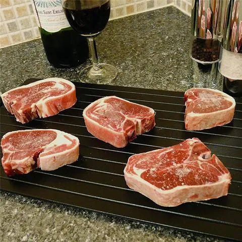 Black aluminium quick defrosting tray for thawing meat and frozen food on a kitchen counter.