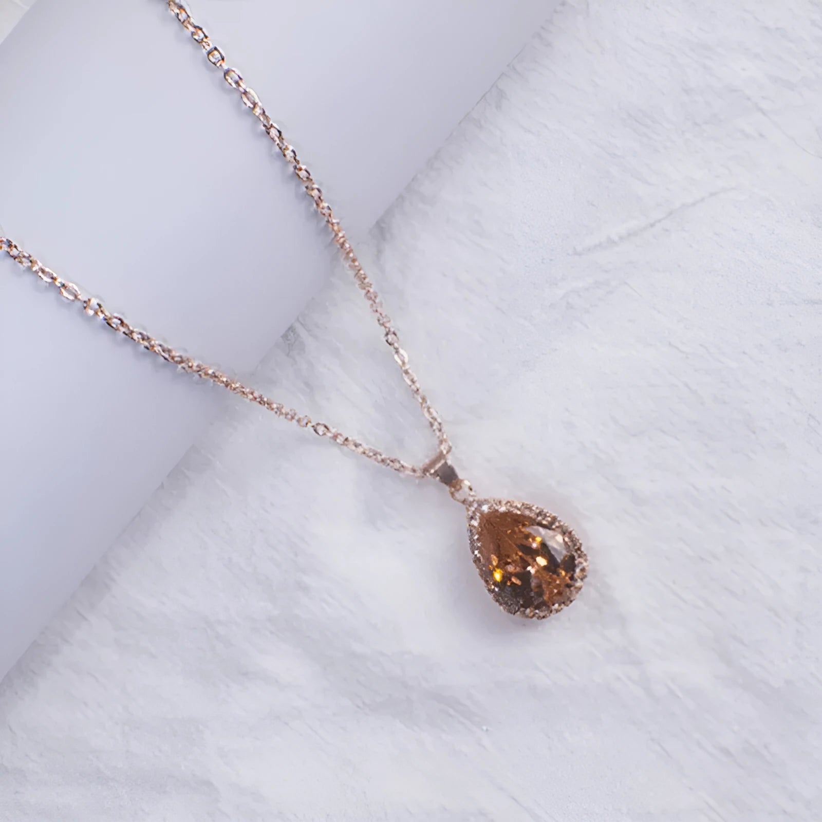 Close-up of a women's rose gold tone drop pendant necklace with pink rhinestone inlay on a model.