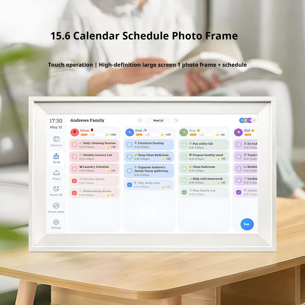 White 15.6 inch smart digital photo frame on a table showing a family photo, with mobile app upload icon.