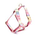 Pink colourful dog harness with gold buckle and heart-shaped stone decoration on a white background.