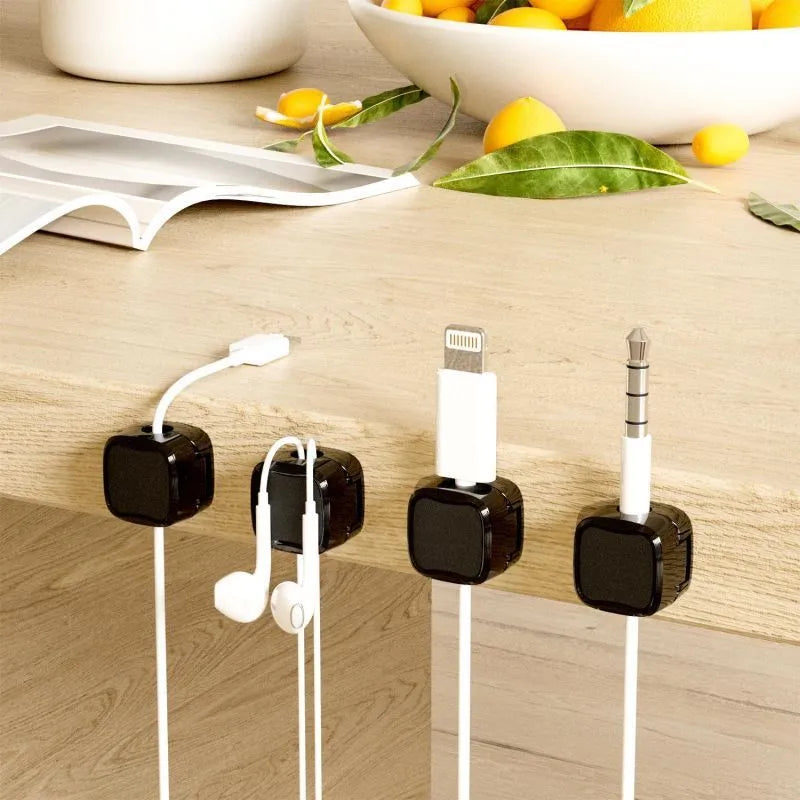 White and black magnetic cable clips with adhesive backing holding a USB cable against a wooden desk edge.