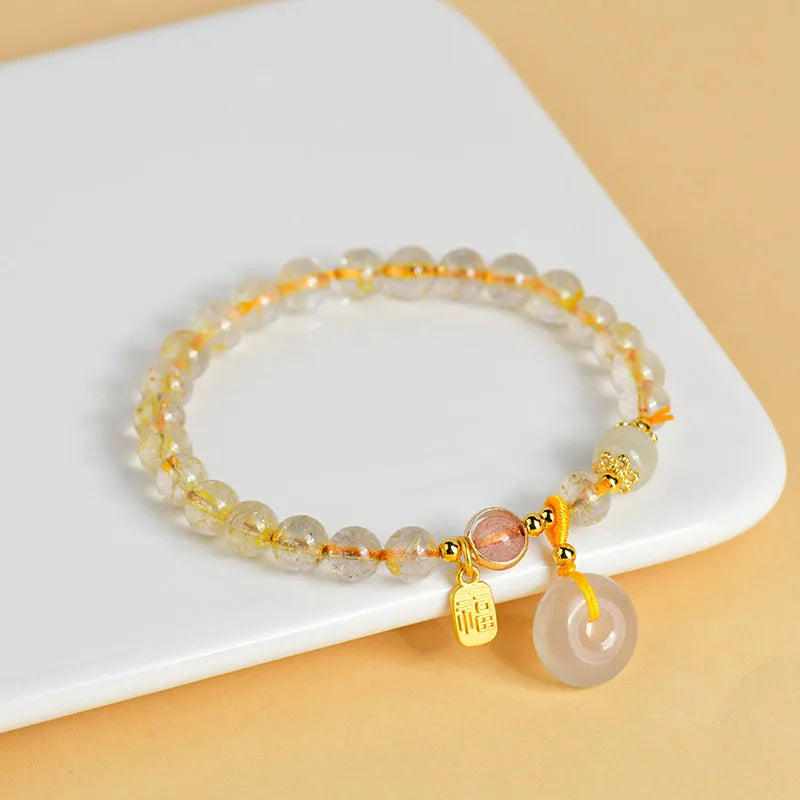 Gold rutilated quartz bracelet with geometric safety buckle and pendant on a white background.