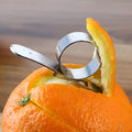 Silver stainless steel finger ring fruit peeler for oranges and pomelos on a kitchen surface.