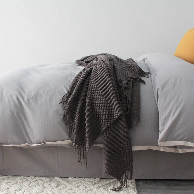 Small light grey polyester nap blanket folded on a sofa, showing its texture and size.