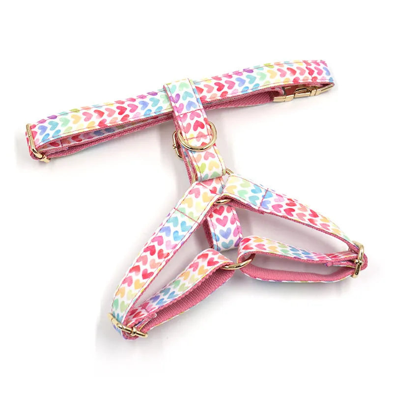 Pink colourful dog harness with gold buckle and heart-shaped stone decoration on a white background.