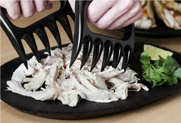 Two black bear claw-shaped meat shredding forks with patterned handles on a kitchen surface.