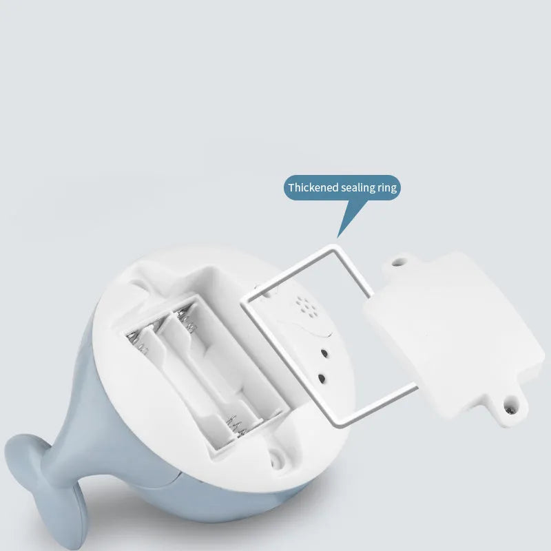 White and blue electric whale bath toy spraying water with flashing lights on a bathroom surface.