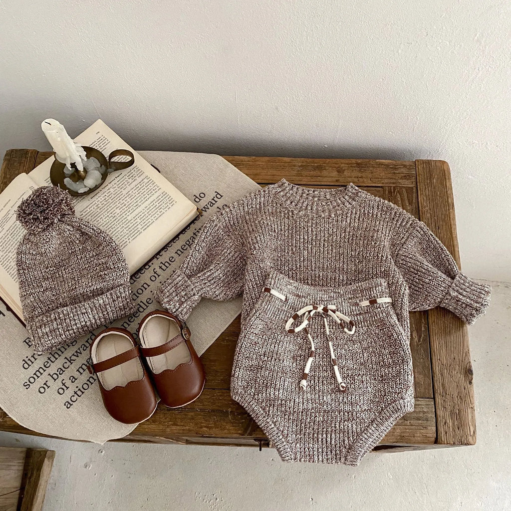 Dark brown knitted 3-piece set for infant girl with pullover blouse, pants, and fur ball hat