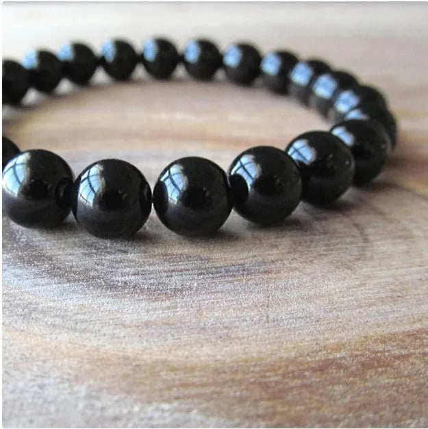 Close-up of a black agate bracelet with 8mm geometric beads on a black elastic cord.
