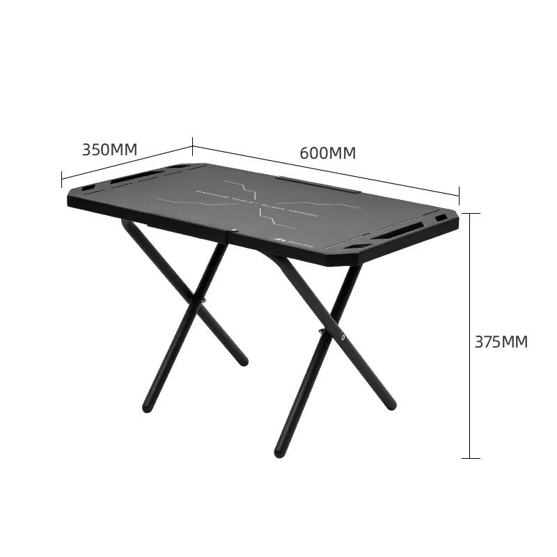 Black folding portable steel camping table on grass with storage bag beside it, 600x350x375mm dimensions visible