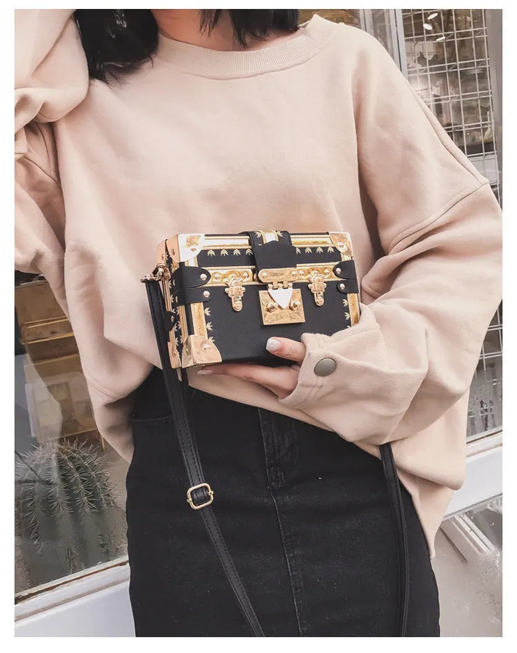 Women's hard black flap handbag with single strap, rivet details, and hasp closure.