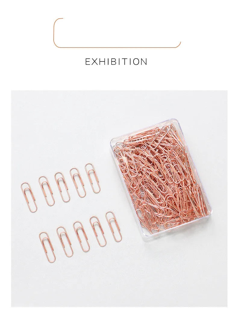 Box of 100 rose gold heart-shaped steel paper clips on a white background.