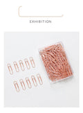 Box of 100 rose gold heart-shaped steel paper clips on a white background.
