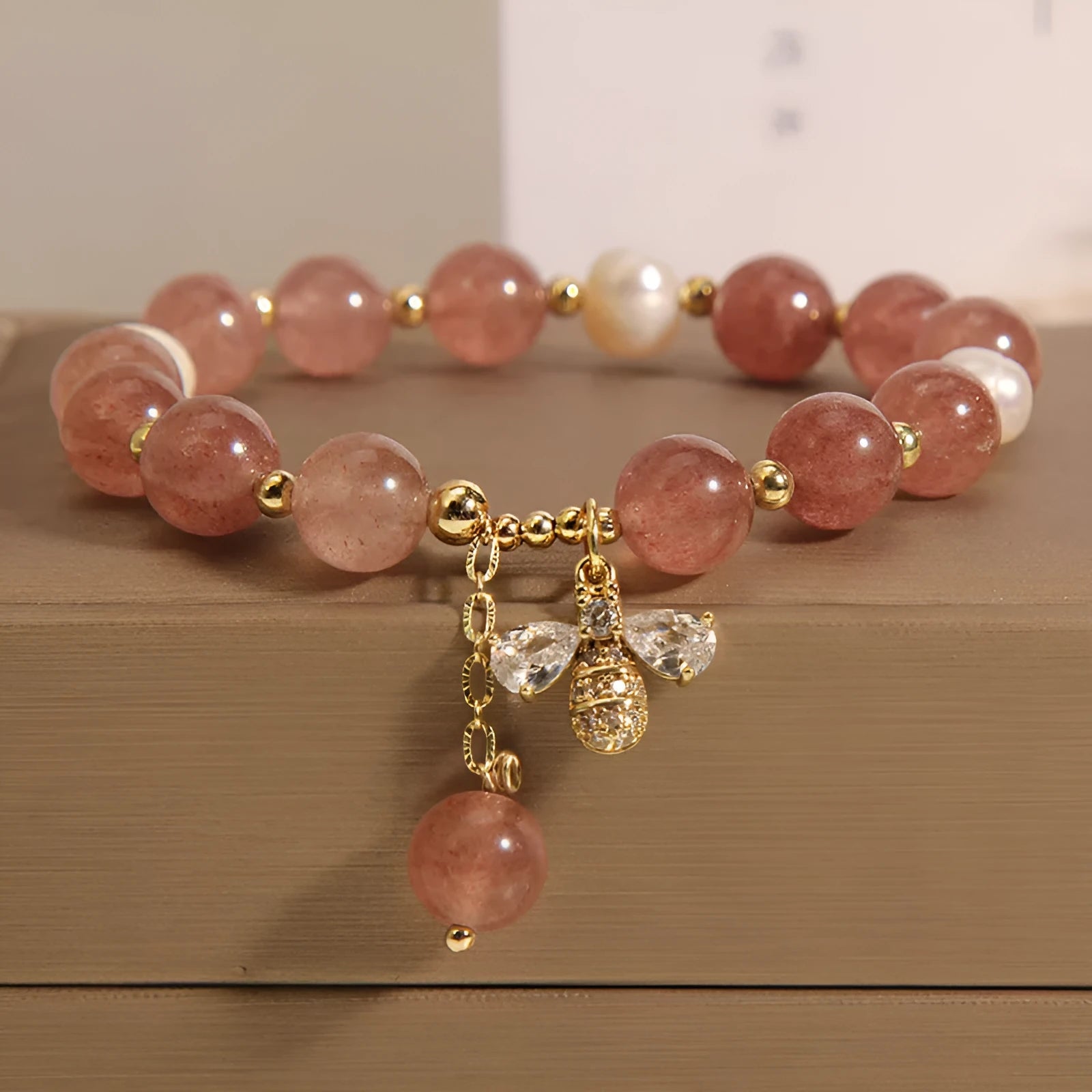 Women's bracelet with strawberry quartz pearls, a zircon bee charm, and alloy links on a wrist.