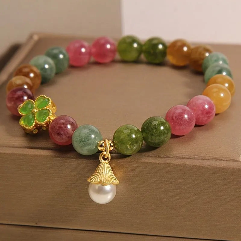 Close-up of a women's silver-toned bracelet with a four-leaf clover charm, pearl pendant, and colourful tourmaline stones.
