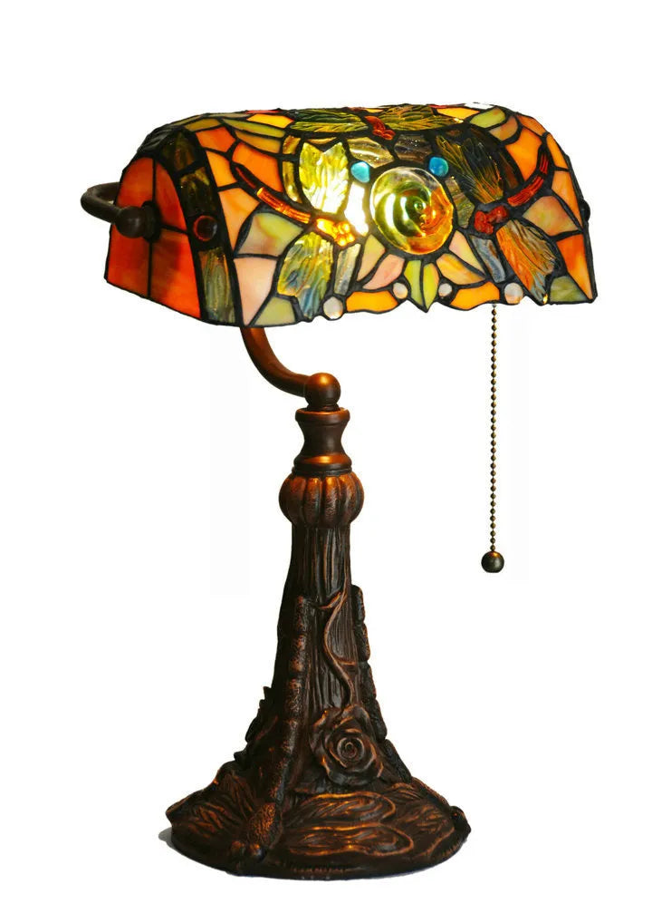 Tiffany style desk lamp with coloured stained glass shade and resin base on a wooden table.