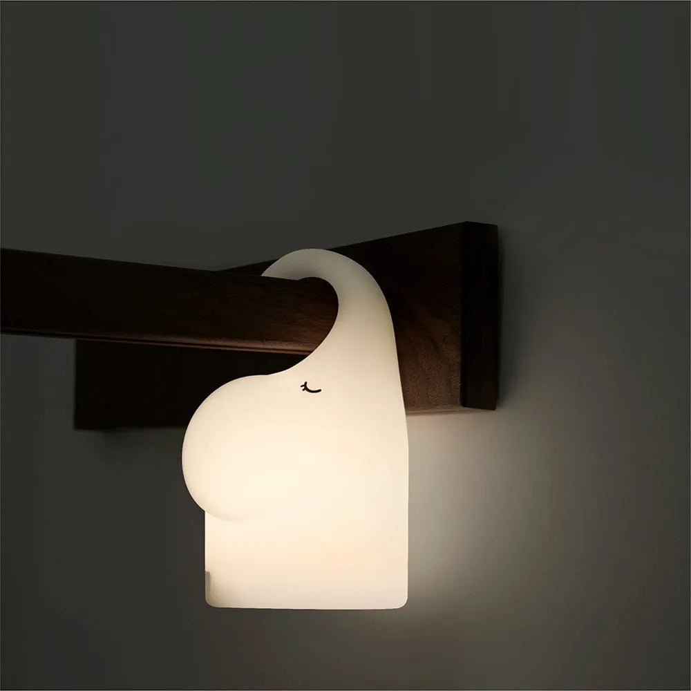 White elephant silicone night light with warm glow on a bedside table.