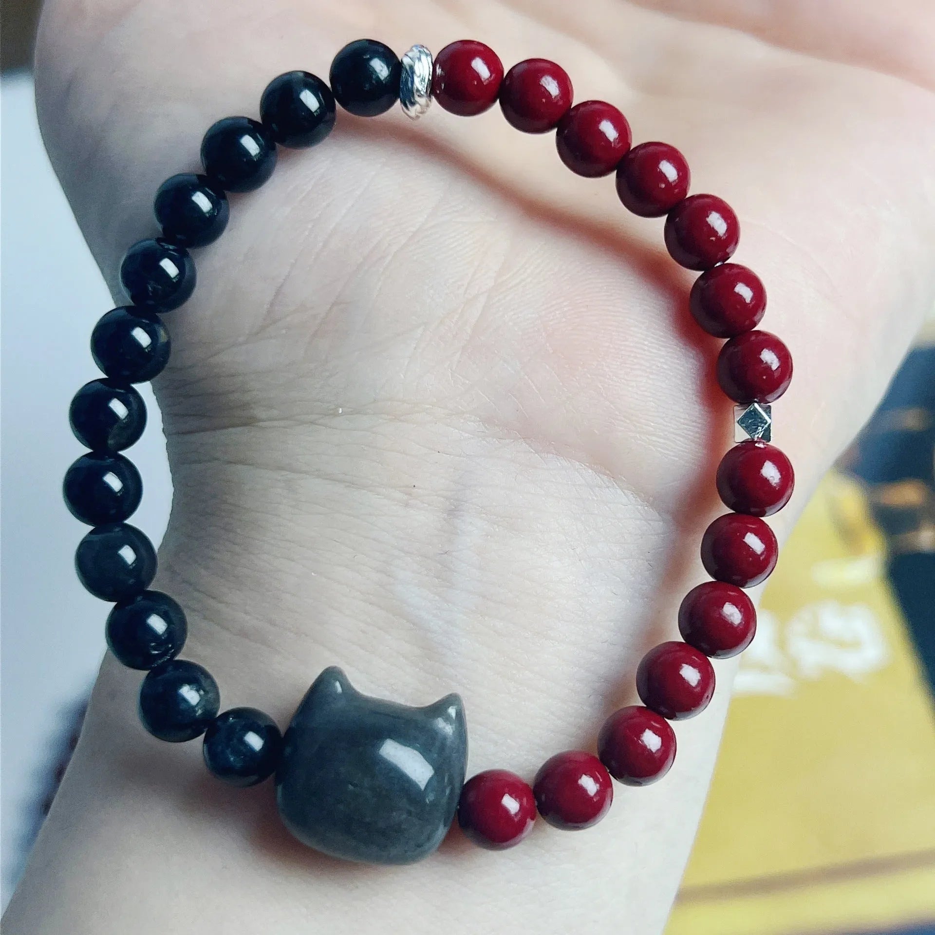 Close-up of handmade obsidian-colour bead bracelet with metal cat charm on adjustable red string.