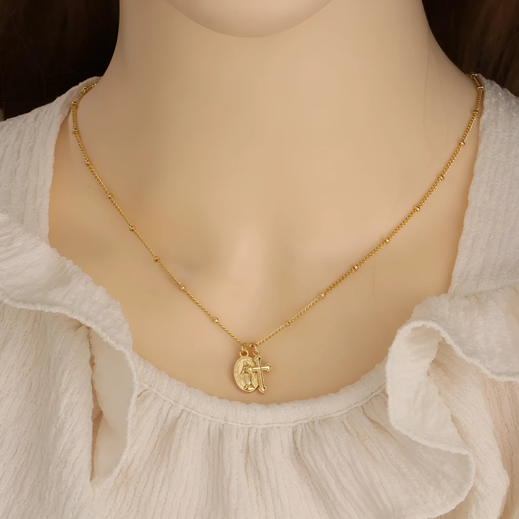 Gold geometric cross Virgin Mary pendant necklace on a chain.