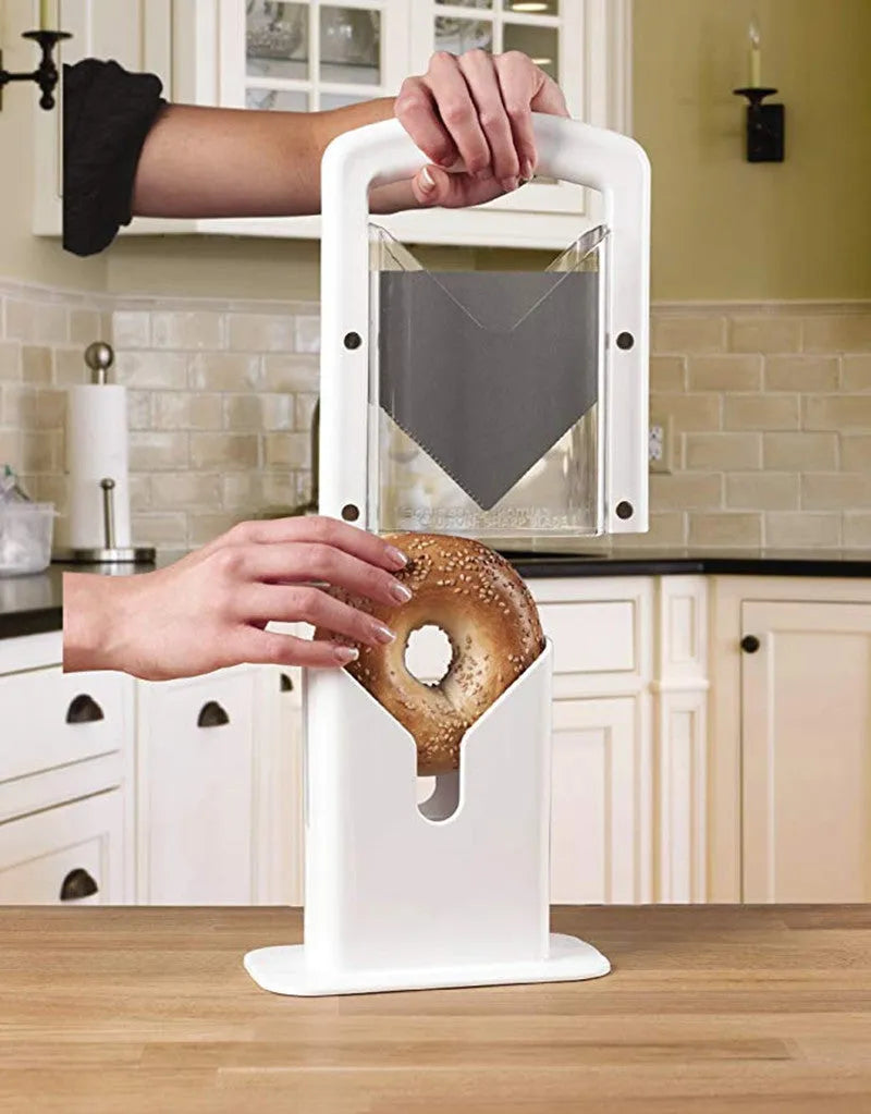 White plastic bagel slicer with acrylic safety shield and stainless steel serrated blade on a kitchen counter