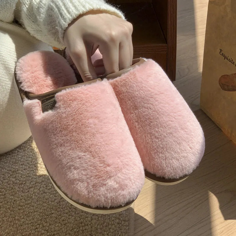 A pair of solid colour winter plush slippers with a PVC sole on a wooden floor.