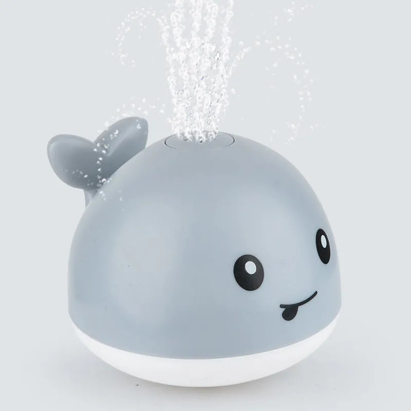 White and blue electric whale bath toy spraying water with flashing lights on a bathroom surface.