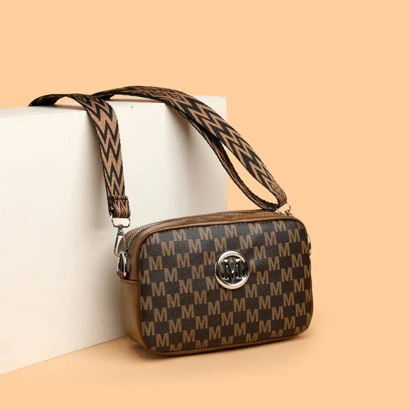 Black crossbody bag with wide strap and a three-dimensional front pocket.