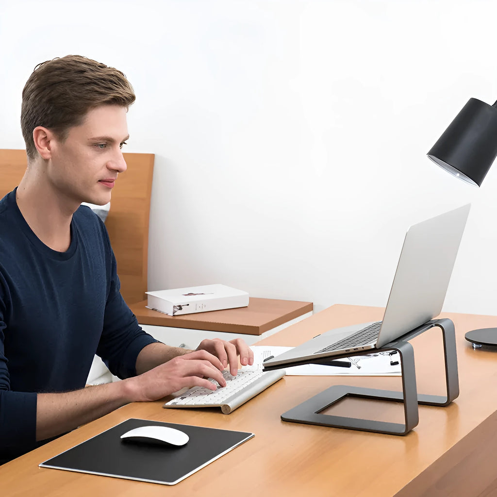 Black aluminium laptop stand with angled platform on a wooden desk