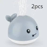 White and blue electric whale bath toy spraying water with flashing lights on a bathroom surface.