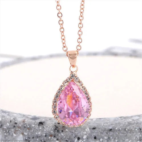 Close-up of a women's rose gold tone drop pendant necklace with pink rhinestone inlay on a model.