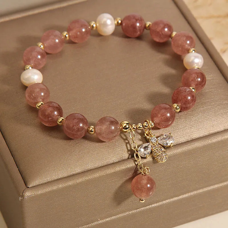 Women's bracelet with strawberry quartz pearls, a zircon bee charm, and alloy links on a wrist.
