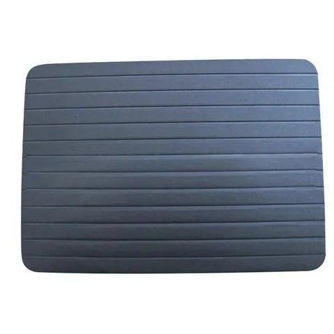 Black aluminium quick defrosting tray for thawing meat and frozen food on a kitchen counter.