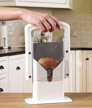 White plastic bagel slicer with acrylic safety shield and stainless steel serrated blade on a kitchen counter