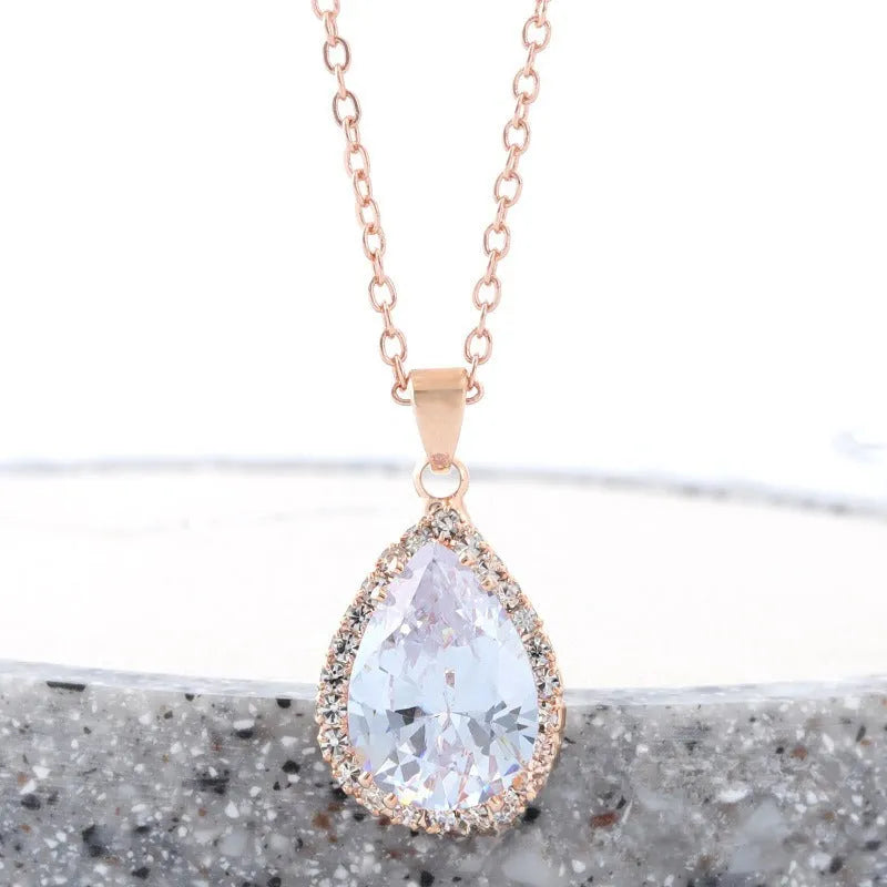 Close-up of a women's rose gold tone drop pendant necklace with pink rhinestone inlay on a model.