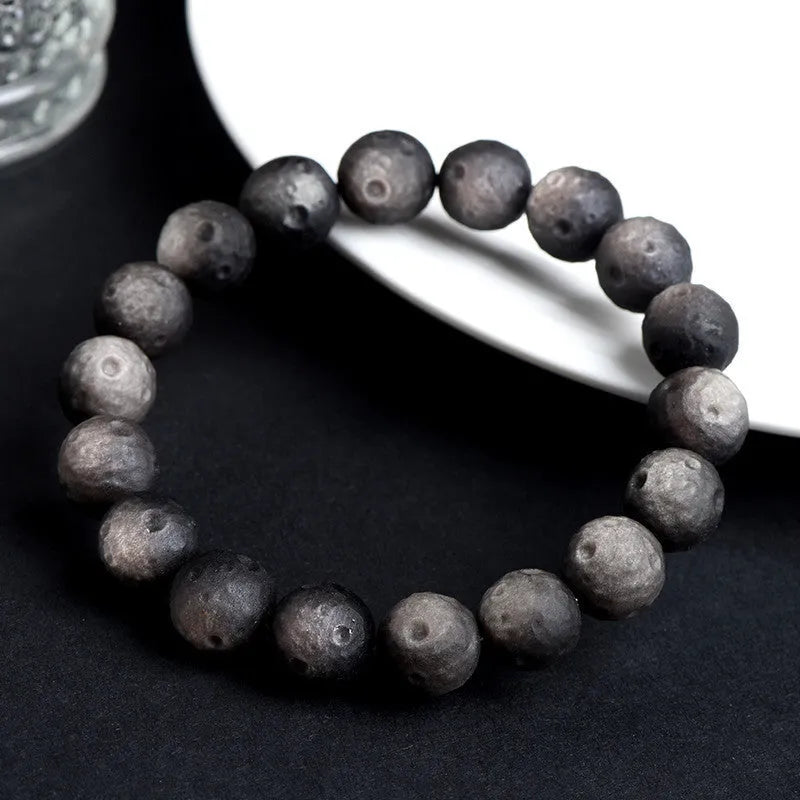 Natural obsidian crater ball bracelet with textured beads on a wrist, showing silver stone meteorite colour variant.