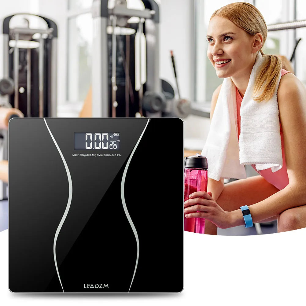 Black electronic digital body scale on a floor with a 180kg maximum capacity.