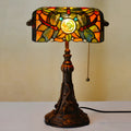 Tiffany style desk lamp with coloured stained glass shade and resin base on a wooden table.