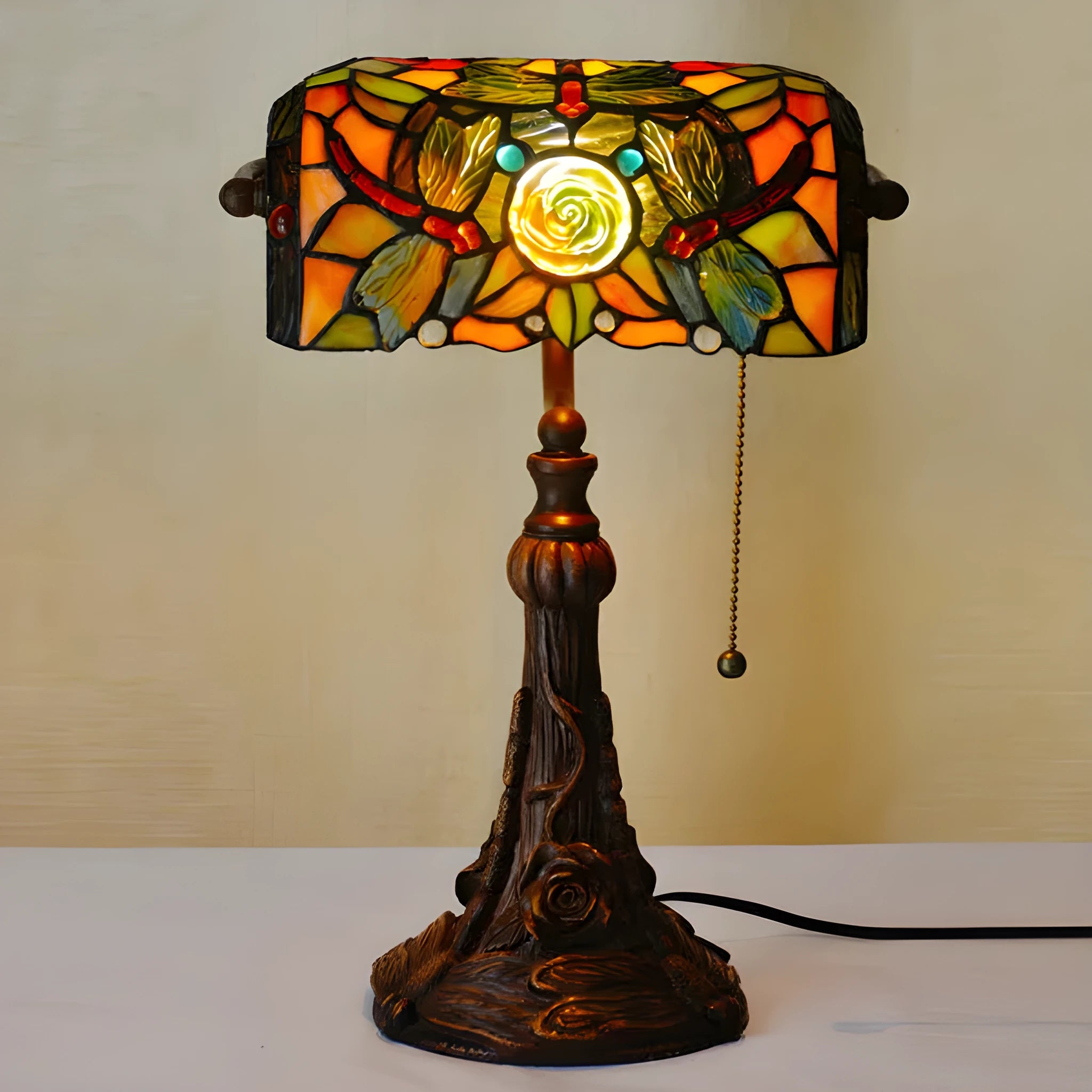 Tiffany style desk lamp with coloured stained glass shade and resin base on a wooden table.