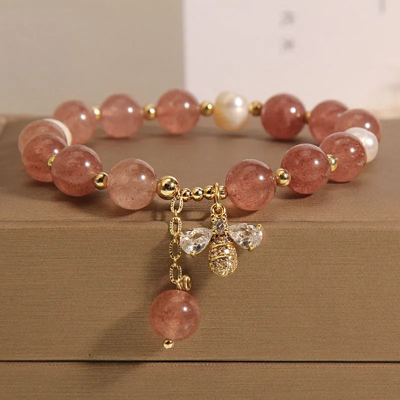 Women's bracelet with strawberry quartz pearls, a zircon bee charm, and alloy links on a wrist.