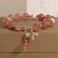 Women's bracelet with strawberry quartz pearls, a zircon bee charm, and alloy links on a wrist.