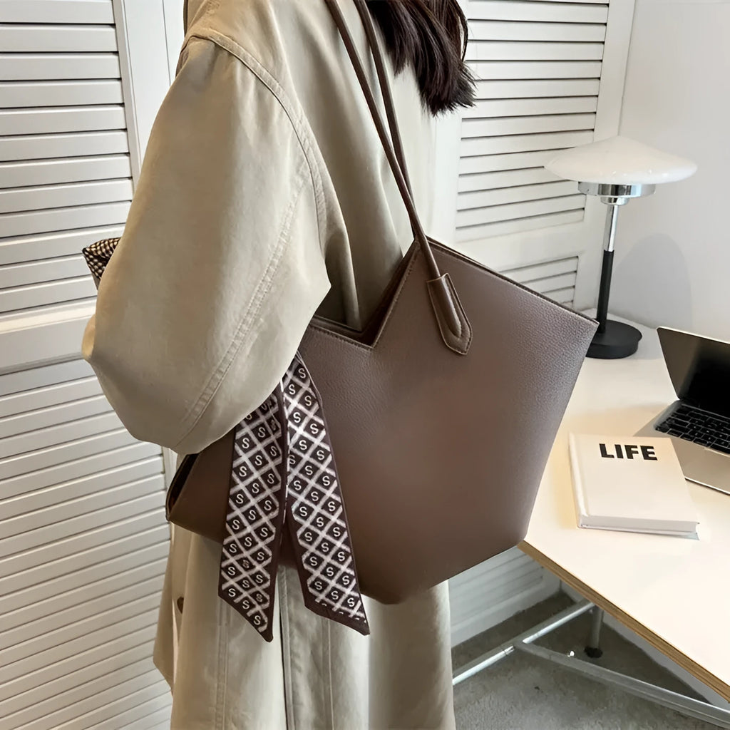 Women's large beige PU shoulder bag with square shape and long strap on a plain background.