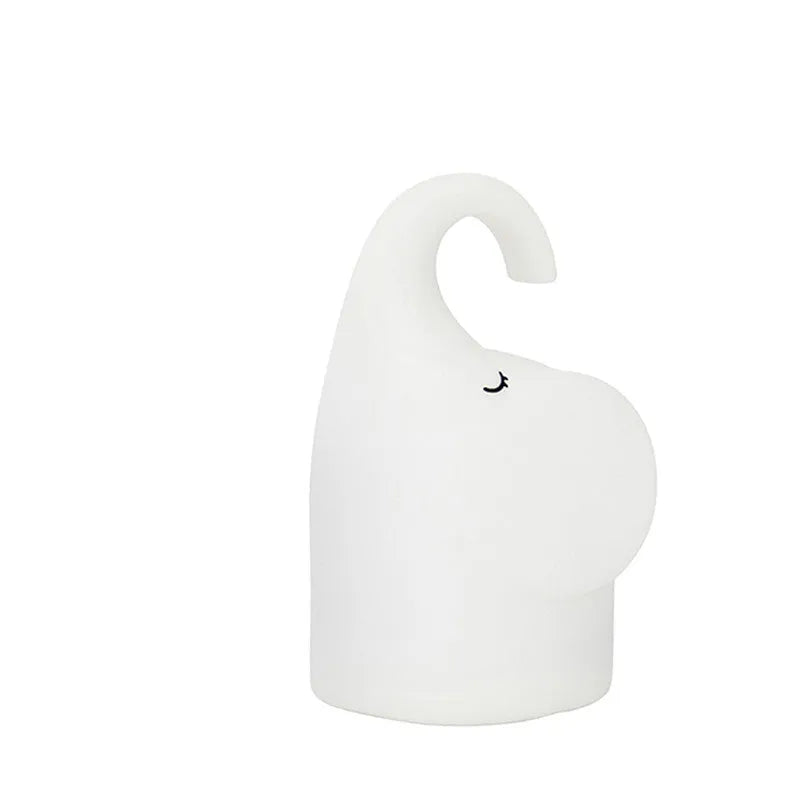 White elephant silicone night light with warm glow on a bedside table.