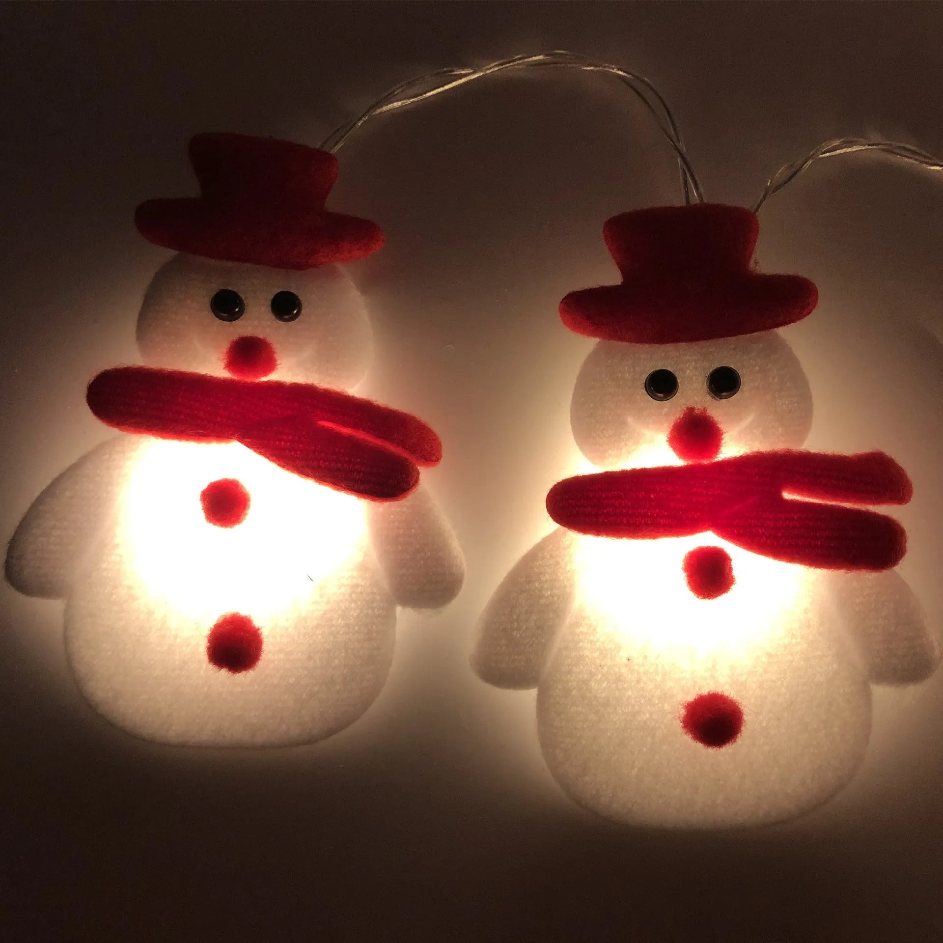 Snowman and elk deer decorative LED Christmas string lights glowing warm white on a green garland.
