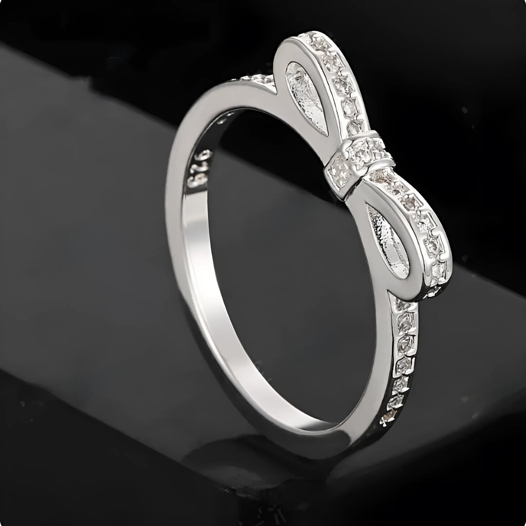Silver bow-shaped ring with sparkling rhinestones and zircon crystals on a finger.
